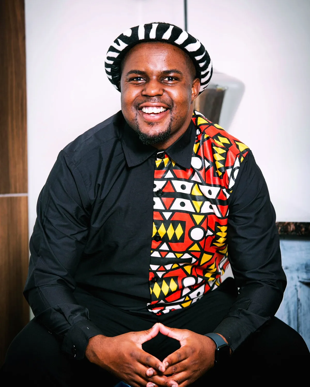 Andrew Tsuro seated, smiling, in a black shirt with a bright patterned panel