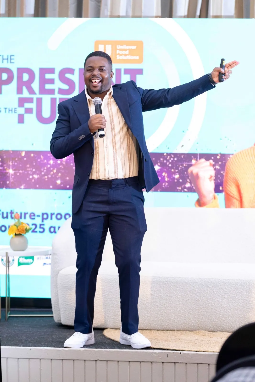 Andrew Tsuro on stage with one arm outstretched, microphone in hand