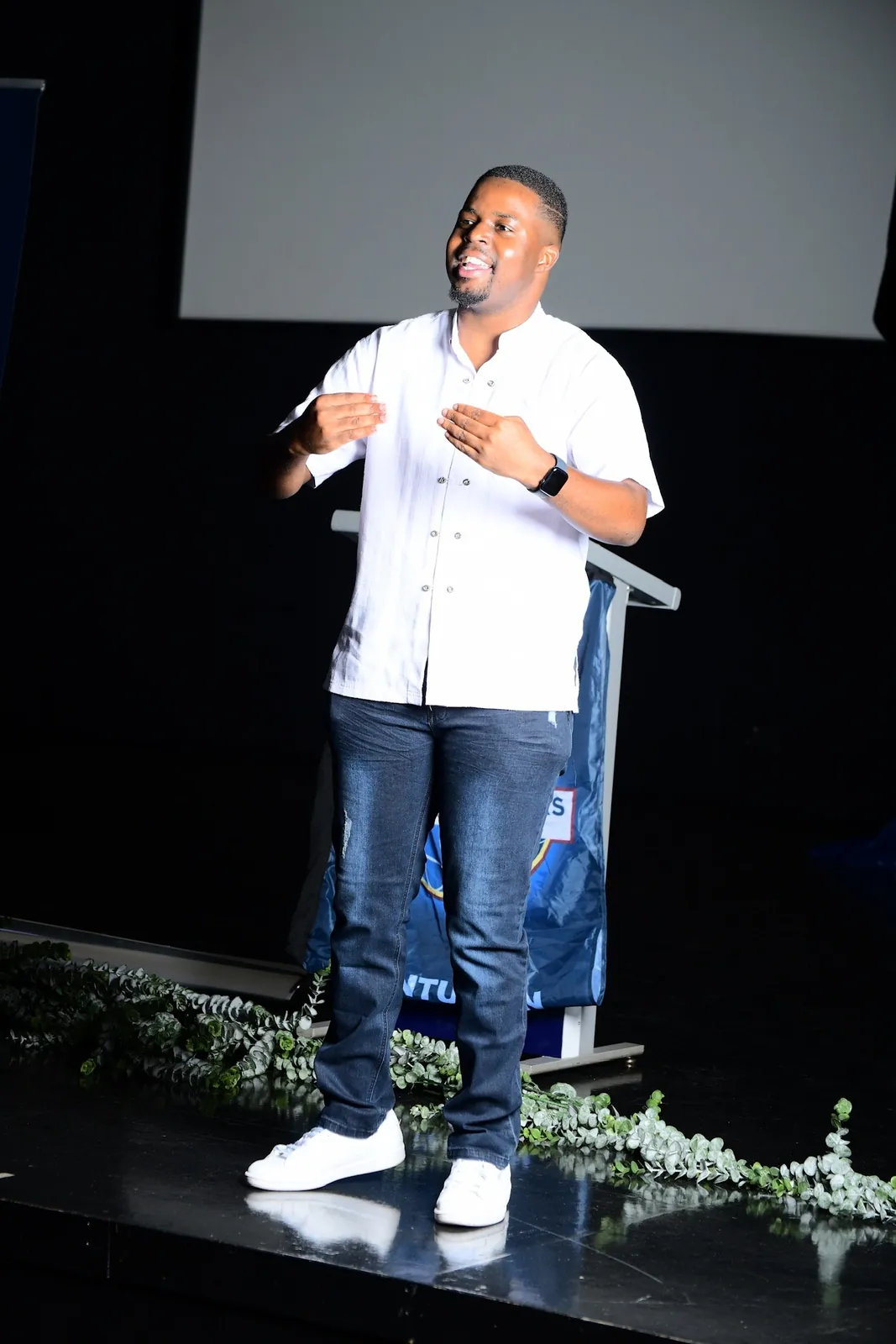 Andrew on a stage in a white shirt, speaking with both hands