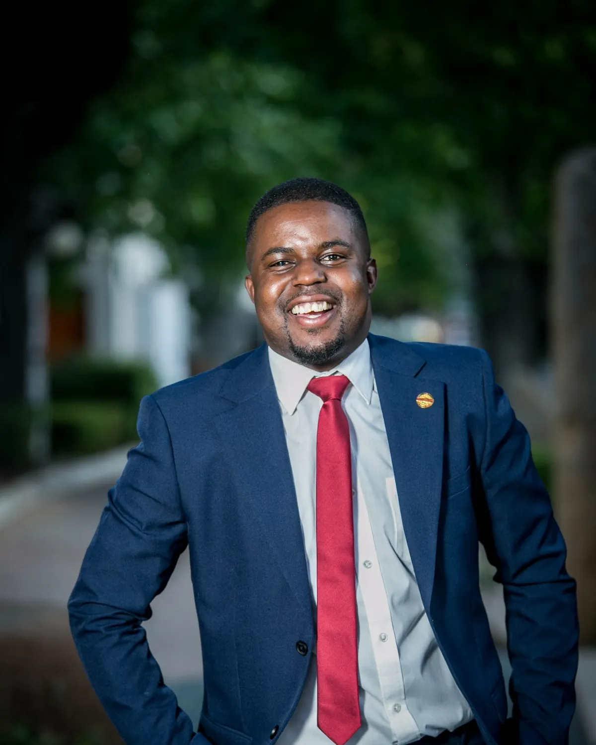 Andrew Tsuro in a blue suit and red tie, smiling, hands in his pockets