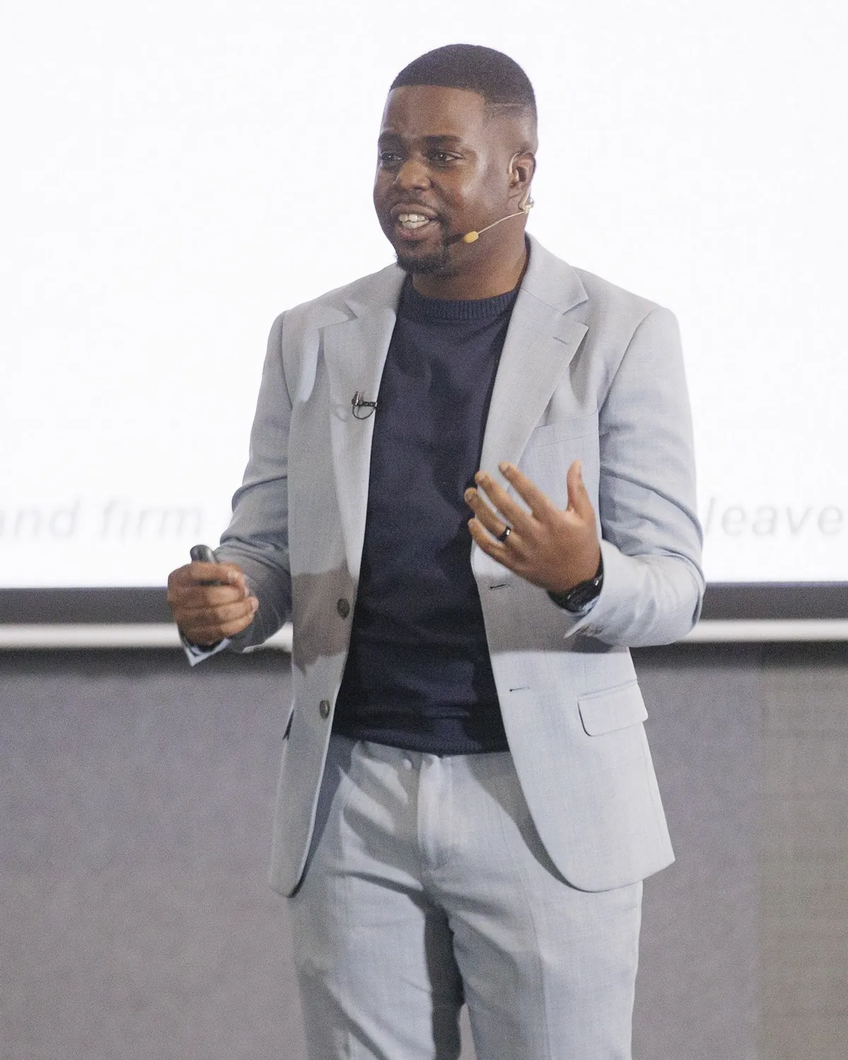 Andrew Tsuro in a grey blazer, speaking with one hand raised