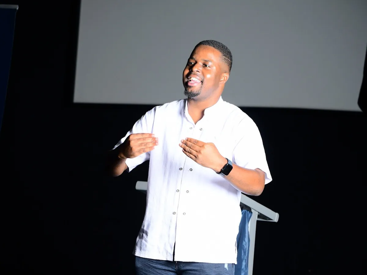 Andrew Tsuro on stage in a white shirt, speaking with both hands