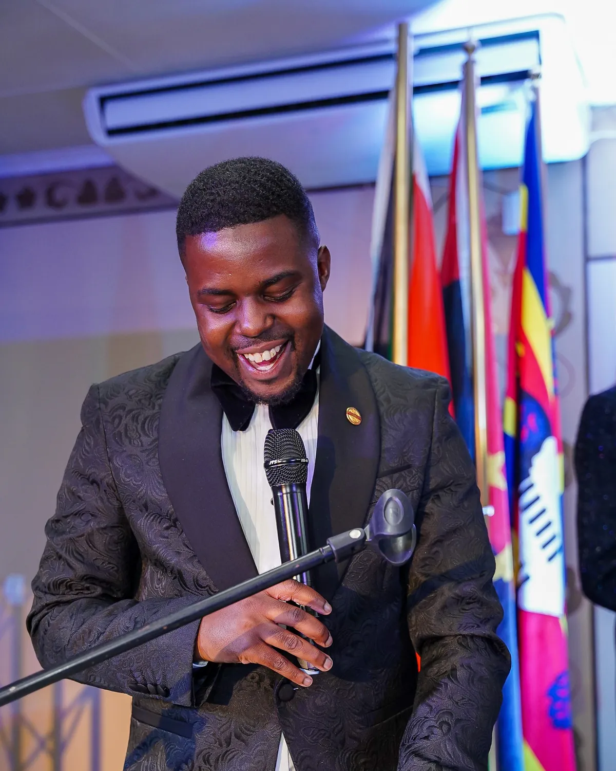 Andrew in a dinner jacket laughing at a microphone