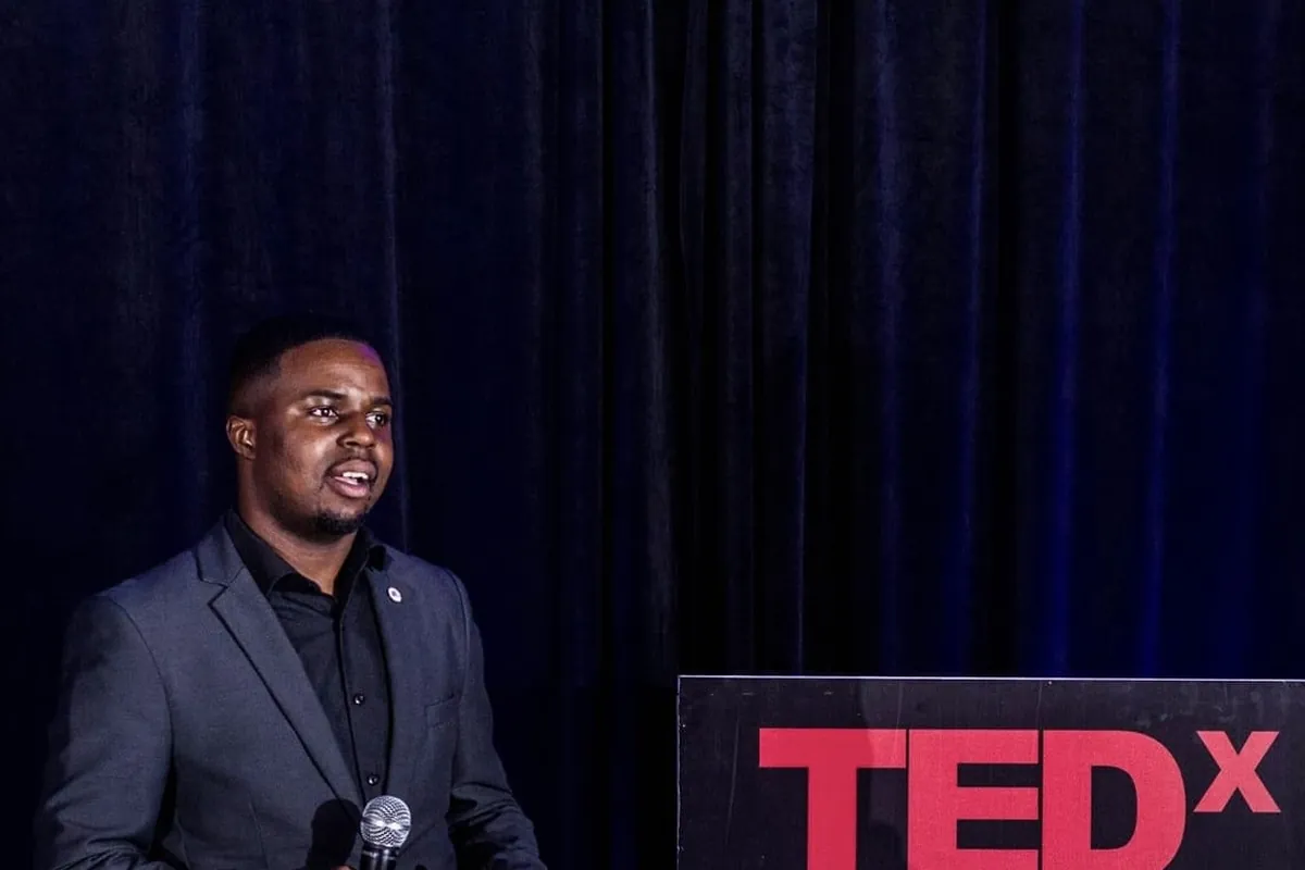 Andrew Tsuro speaking beside a TEDx stage sign